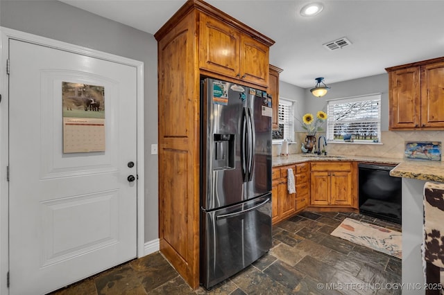 kitchen featuring dishwasher, sink, tasteful backsplash, light stone counters, and stainless steel refrigerator with ice dispenser