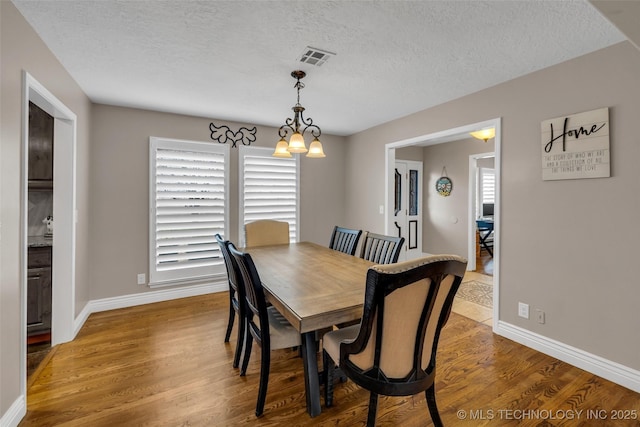 dining area with a textured ceiling, light wood-type flooring, and a notable chandelier