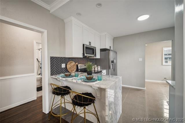 kitchen with ornamental molding, light stone counters, appliances with stainless steel finishes, a kitchen bar, and white cabinetry