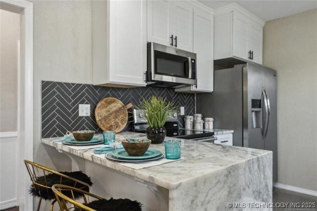 kitchen featuring decorative backsplash, light stone countertops, stainless steel appliances, white cabinets, and a breakfast bar area