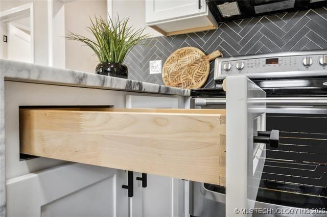 interior details with backsplash, range hood, white cabinets, and stainless steel range with electric stovetop