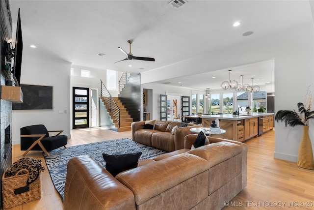 living room with light wood-type flooring, ceiling fan with notable chandelier, a stone fireplace, and sink