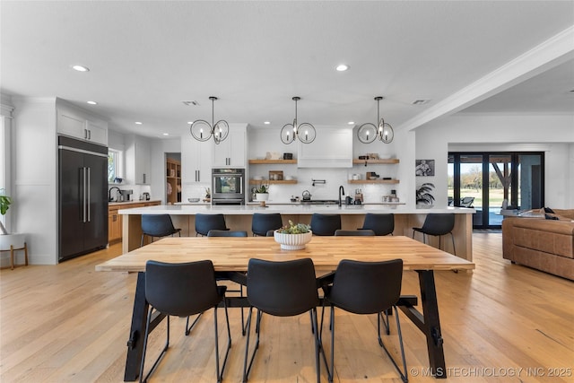 dining area with a chandelier, sink, ornamental molding, and light wood-type flooring