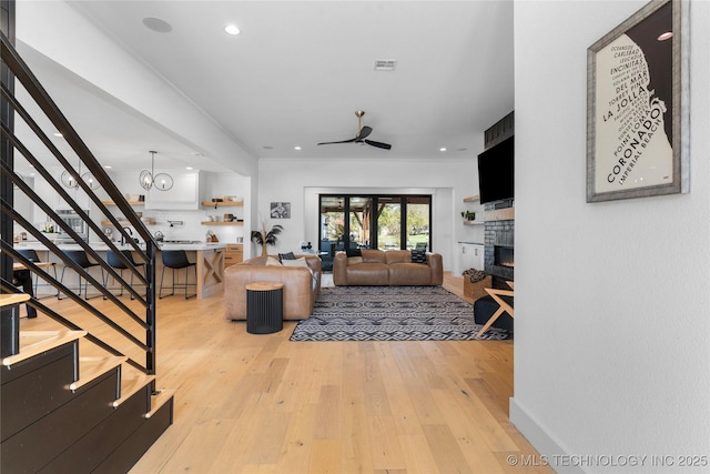 living room featuring ceiling fan, light wood-style flooring, a fireplace, visible vents, and stairway