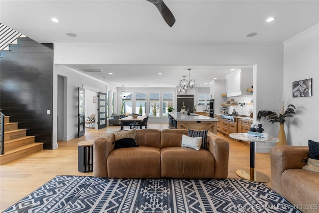 living room with crown molding, light hardwood / wood-style flooring, a chandelier, and sink