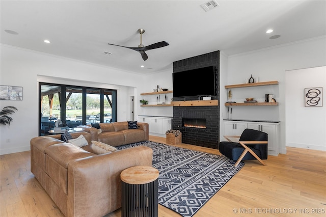 living room with light wood-type flooring, a brick fireplace, ceiling fan, and ornamental molding