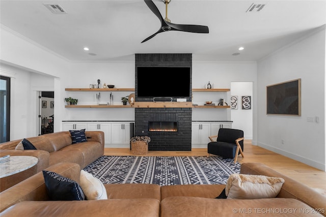 living room with light hardwood / wood-style floors, a brick fireplace, ceiling fan, and crown molding