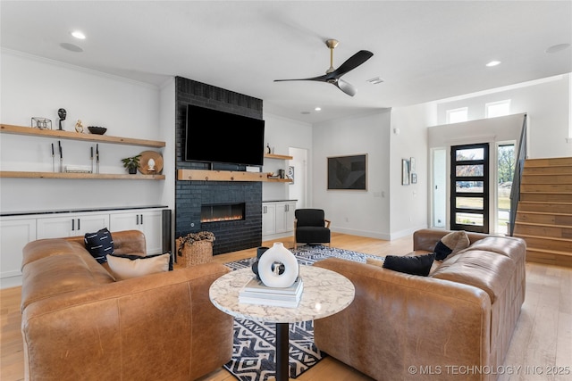 living room with a fireplace, ceiling fan, light hardwood / wood-style flooring, and ornamental molding