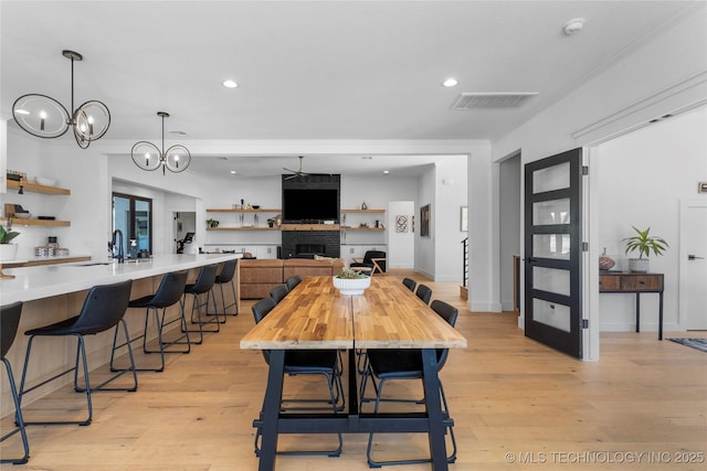 dining area featuring ceiling fan with notable chandelier, a large fireplace, light hardwood / wood-style flooring, and crown molding