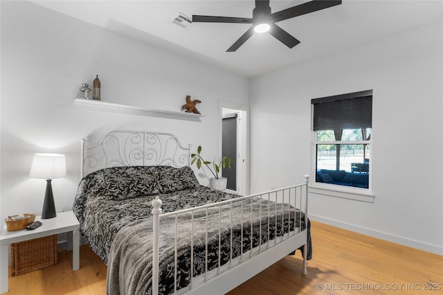 bedroom featuring a ceiling fan, wood finished floors, visible vents, and baseboards