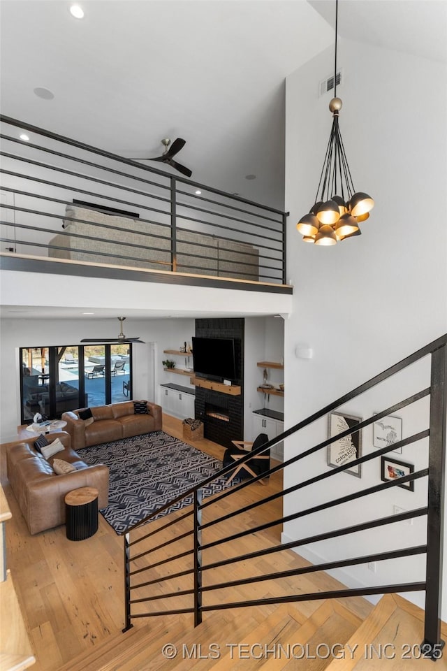 living room featuring ceiling fan with notable chandelier, a towering ceiling, parquet floors, and a brick fireplace