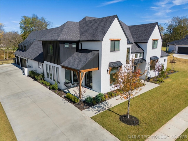 view of front facade with driveway, a shingled roof, a front yard, board and batten siding, and stucco siding