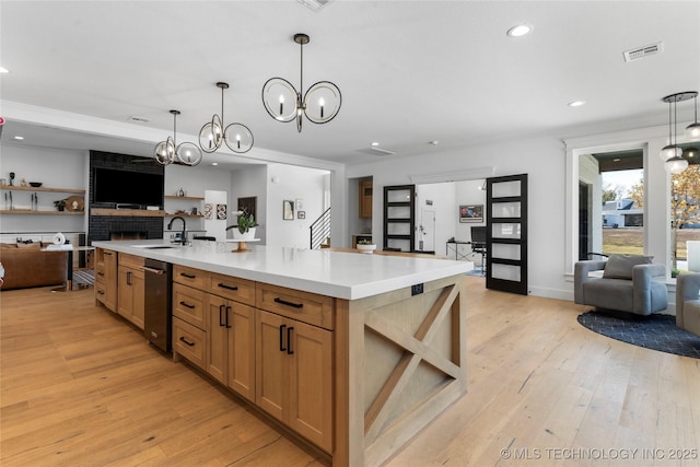 kitchen with a fireplace, an island with sink, hanging light fixtures, and an inviting chandelier