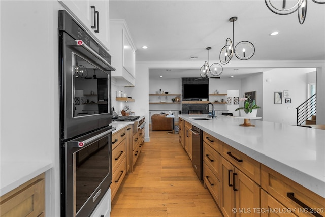 kitchen with white cabinets, open floor plan, double wall oven, light countertops, and a sink