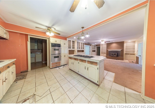 kitchen with a center island, a wood stove, light carpet, hanging light fixtures, and appliances with stainless steel finishes