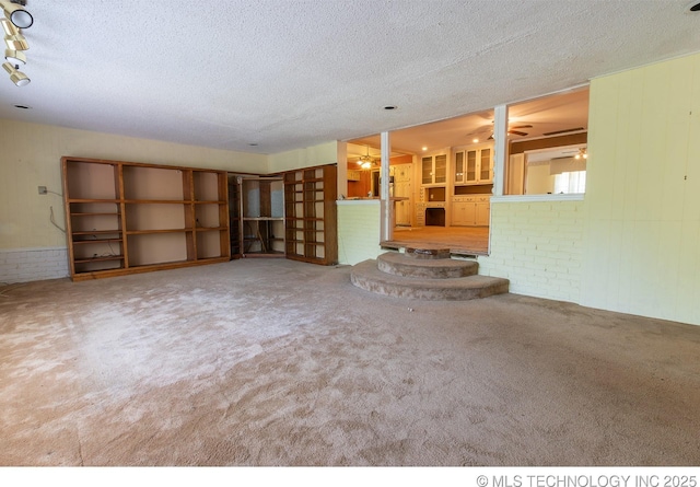 unfurnished living room with ceiling fan, carpet floors, brick wall, and a textured ceiling