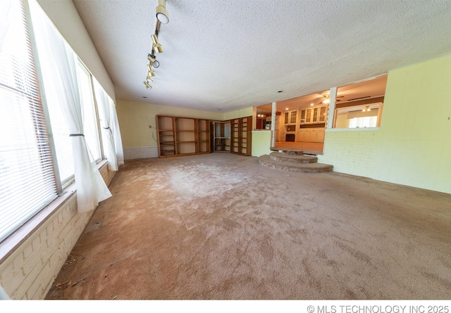 unfurnished living room featuring carpet, a textured ceiling, track lighting, and brick wall