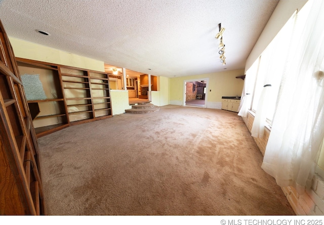 unfurnished living room with a textured ceiling, rail lighting, and light carpet