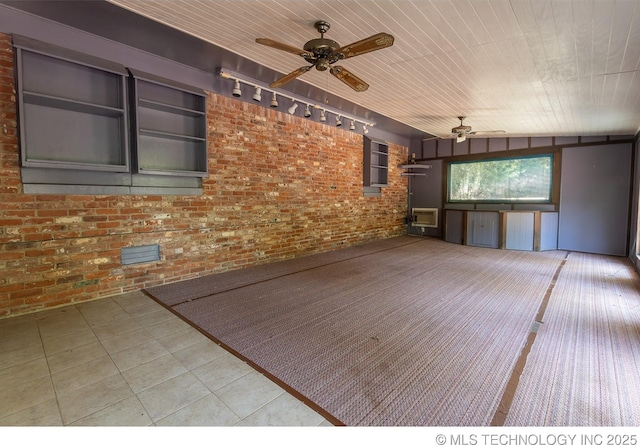 exterior space featuring rail lighting, ceiling fan, and brick wall