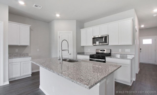 kitchen with sink, stainless steel appliances, light stone counters, an island with sink, and white cabinets