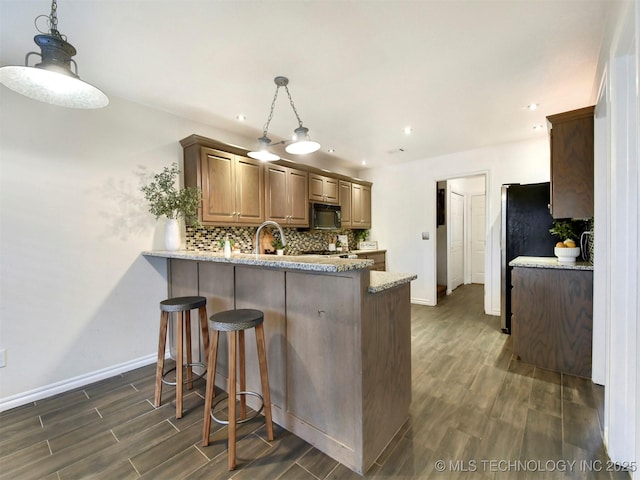 kitchen featuring kitchen peninsula, light stone countertops, tasteful backsplash, decorative light fixtures, and fridge