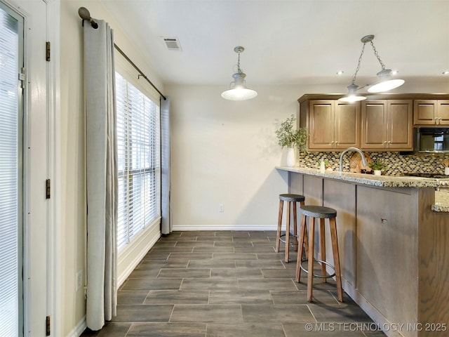 kitchen featuring sink, hanging light fixtures, decorative backsplash, light stone countertops, and a kitchen bar