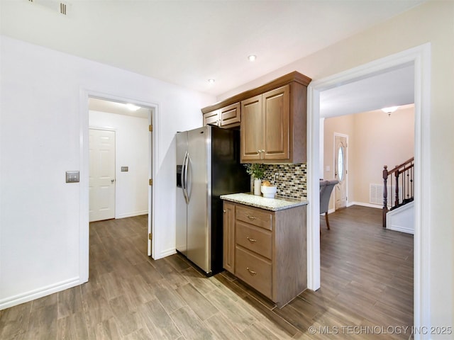 kitchen with light stone countertops, wood-type flooring, stainless steel refrigerator with ice dispenser, and tasteful backsplash