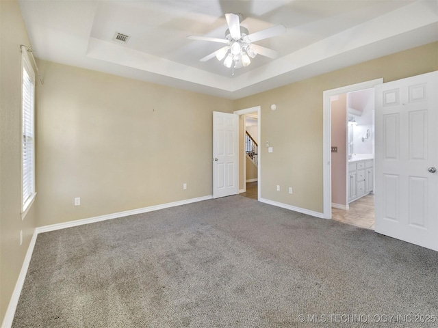 unfurnished bedroom featuring a tray ceiling, ensuite bath, ceiling fan, and light carpet