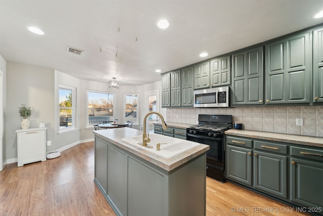 kitchen featuring decorative backsplash, a kitchen island with sink, black gas stove, and green cabinetry