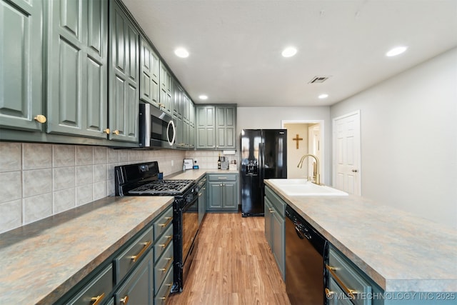 kitchen featuring backsplash, black appliances, green cabinets, sink, and light hardwood / wood-style floors