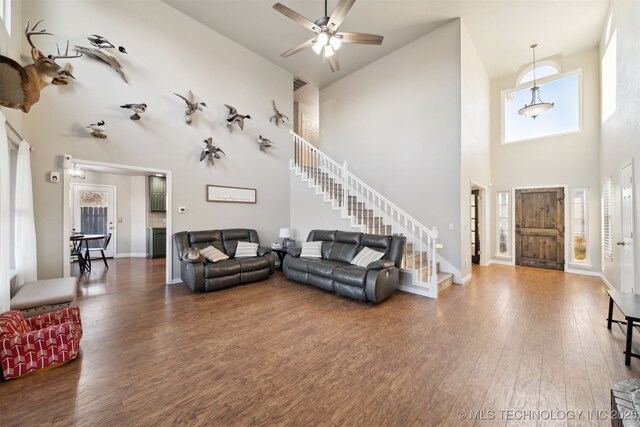 living room with ceiling fan, dark wood-type flooring, and a high ceiling