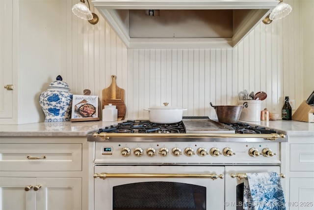 kitchen with high end range, white cabinets, light stone counters, and wooden walls