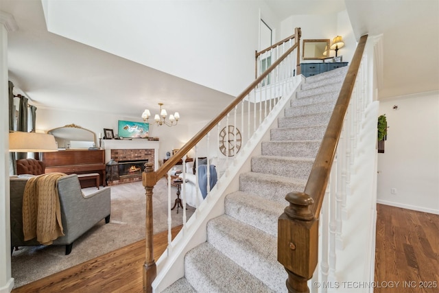 stairs featuring an inviting chandelier, wood-type flooring, and a brick fireplace