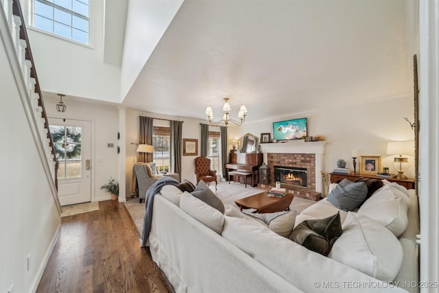 living room with an inviting chandelier, a brick fireplace, and dark wood-type flooring