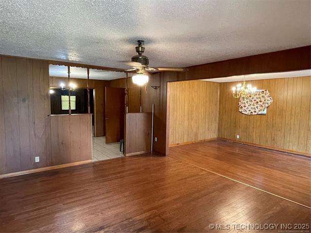 spare room featuring ceiling fan with notable chandelier, wood walls, light wood-type flooring, and a textured ceiling