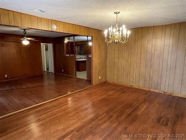 interior space featuring dark hardwood / wood-style flooring, ceiling fan with notable chandelier, and wooden walls