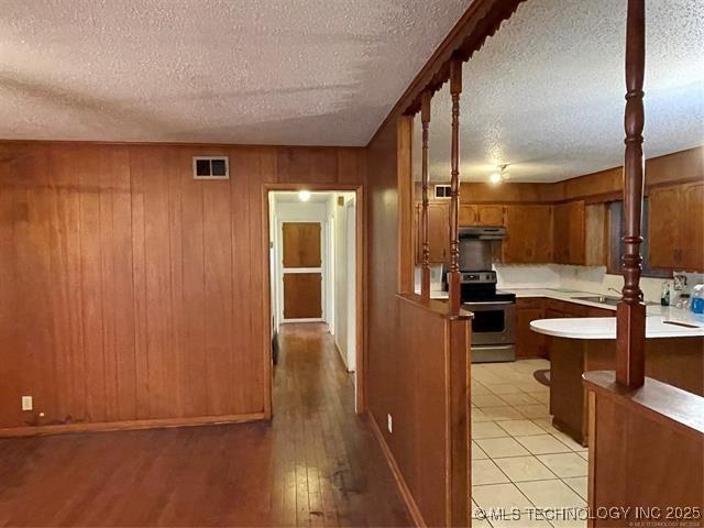 kitchen with a textured ceiling, electric range, and wooden walls