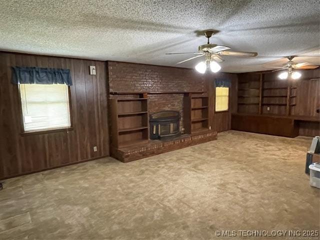 unfurnished living room featuring ceiling fan, a brick fireplace, a textured ceiling, wooden walls, and carpet