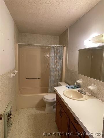 full bathroom featuring vanity, shower / bathtub combination with curtain, a textured ceiling, and toilet