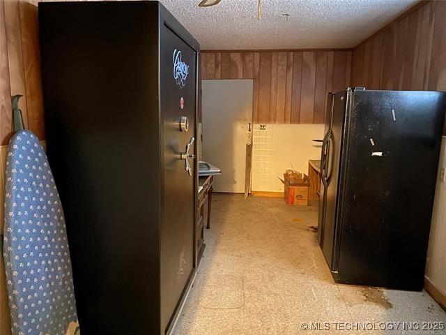 kitchen with black refrigerator, a textured ceiling, and wood walls