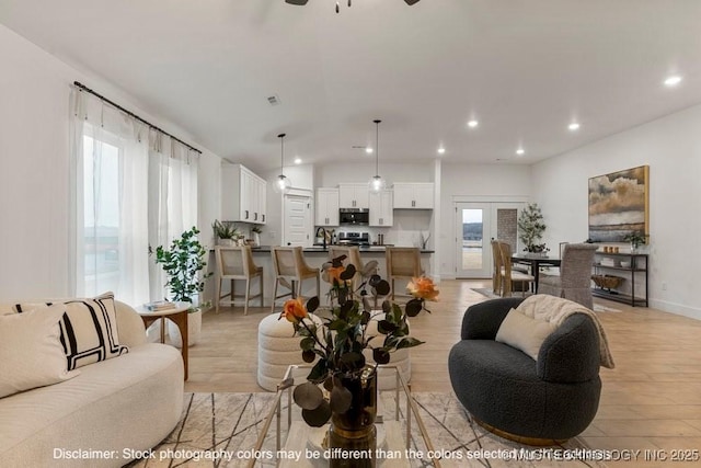 living room with baseboards, visible vents, lofted ceiling, light wood-type flooring, and recessed lighting