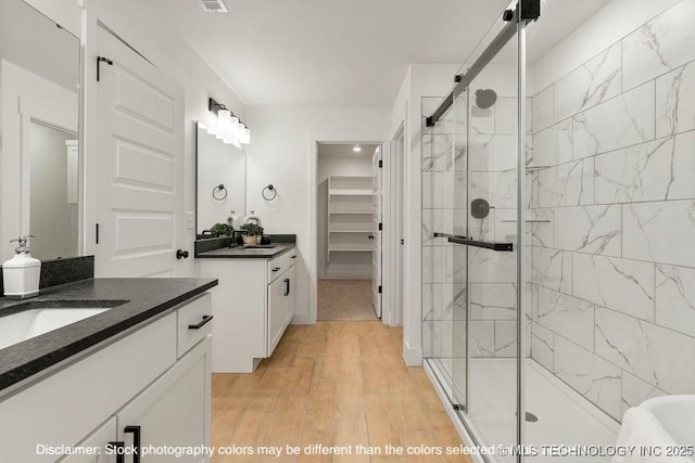 bathroom with two vanities, a spacious closet, a sink, a shower stall, and wood finished floors