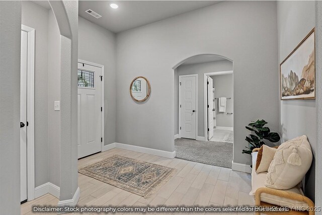 foyer entrance featuring light wood-type flooring, arched walkways, visible vents, and baseboards