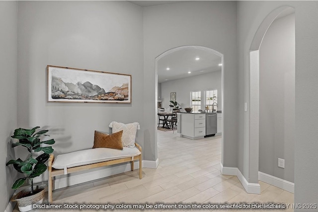 hallway with light wood finished floors, baseboards, and arched walkways