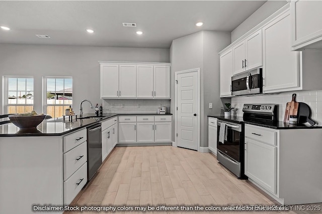 kitchen with dark countertops, visible vents, appliances with stainless steel finishes, white cabinetry, and a peninsula