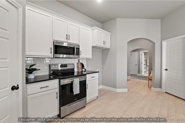 kitchen with stainless steel appliances, dark countertops, white cabinets, and arched walkways