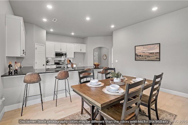 dining room with light wood-type flooring, arched walkways, baseboards, and recessed lighting