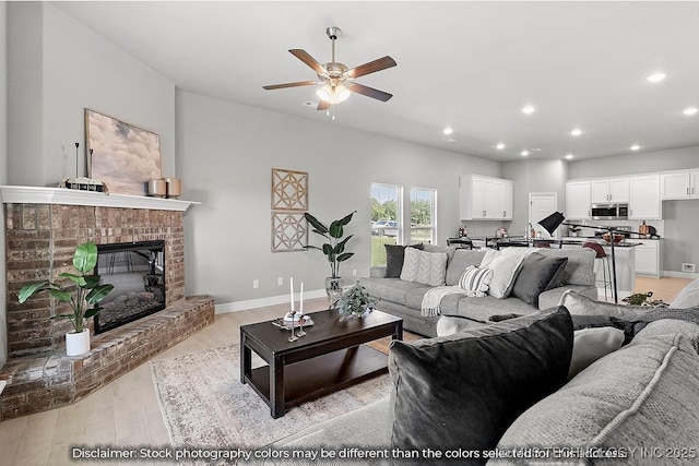 living room featuring baseboards, light wood-type flooring, a fireplace, and recessed lighting