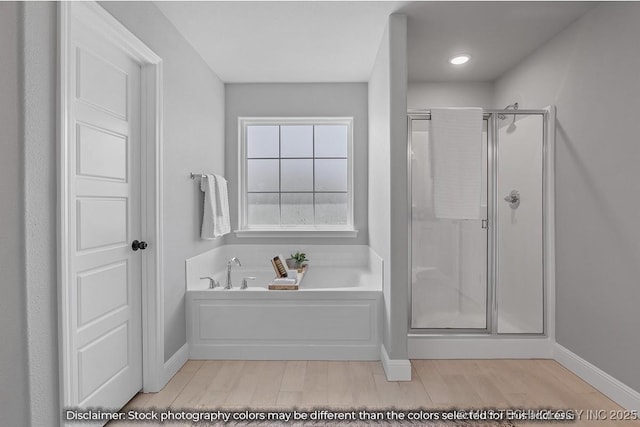 bathroom with a stall shower, wood finished floors, a bath, and baseboards