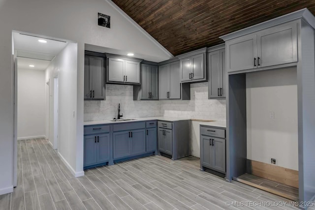 kitchen with tasteful backsplash, gray cabinetry, sink, and vaulted ceiling